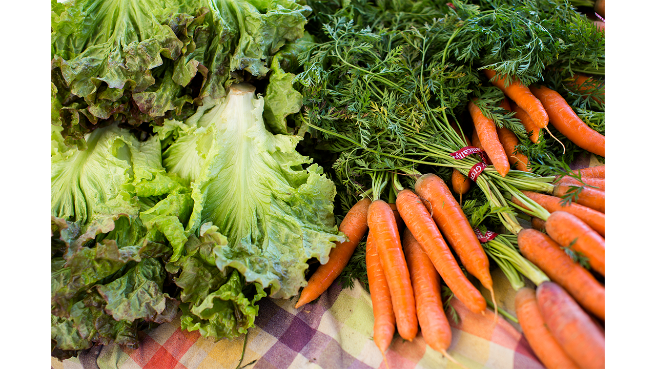 bunches of lettuces and carrots displayed at a California farmer's market on a tablecloth